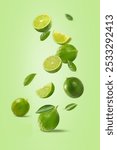 Fresh ripe lime with slices and leaves falling in the air on light green background.