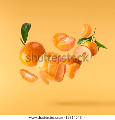 Fresh ripe mandarine with leaves falling in the air. Cut and whole mandarine isolated on yellow background. Food levitation concept. High resolution image