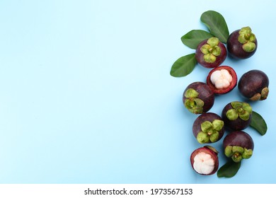 Fresh ripe mangosteen fruits with green leaves on light blue background, flat lay. Space for text