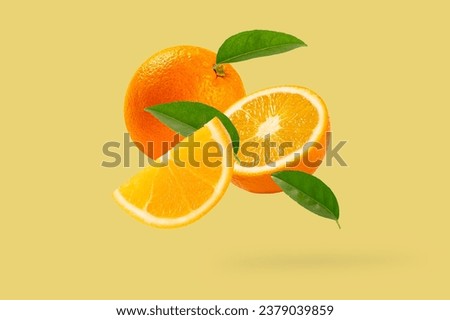 Fresh ripe orange with green leaves falling in the air on yellow background.
