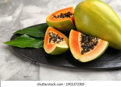 Fresh ripe papaya fruits with green leaves on grey table