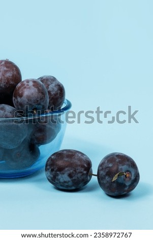 Fresh ripe plums in a blue glass bowl on a blue background
