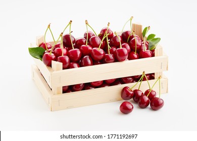 Fresh, ripe sweet cherries in small wooden crate on white background.