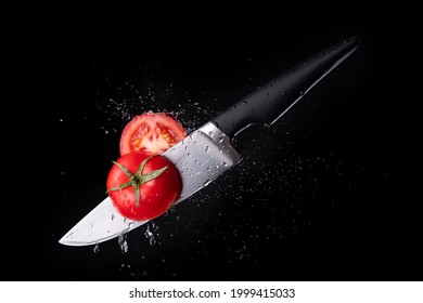 Fresh ripe tomato cutting with a knife and flying in motion on the black background with red splashes