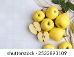 Fresh ripe yellow apples and leaves on white tiled table, flat lay. Space for text