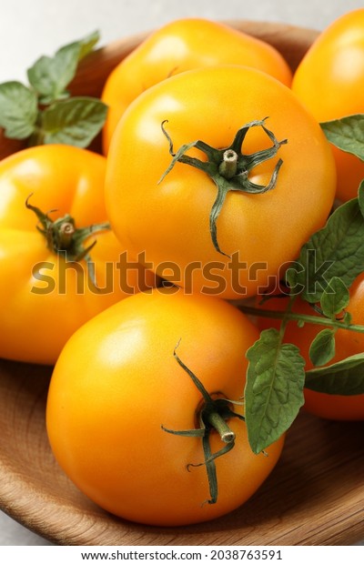 Fresh ripe yellow tomatoes with leaves in wooden\
bowl, closeup