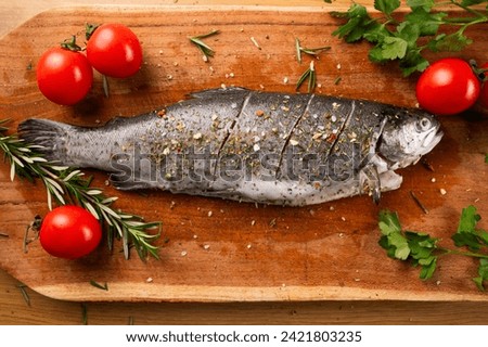Fresh river trout with tomatoes and herbs de Provence on a kitchen wooden board. Cooking delicious and healthy food at home.Fresh fish trout and ingredients for cooking. Raw fish.