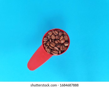 Fresh Roast Whole Coffee Beans In A Red Plastic Coffee Spoon Isolated On Blue Background.