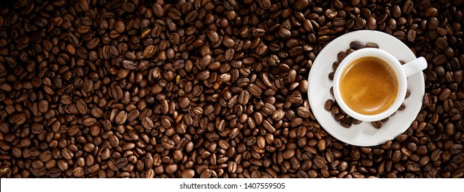 Fresh roasted coffee bean background with a cup of hot frothy espresso placed to the right side in a wide panorama banner with copy space - Powered by Shutterstock