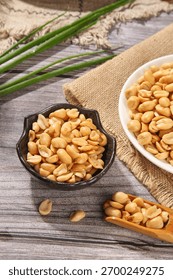 Fresh roasted peanuts served in rustic bowls on wooden background, ready to eat as healthy snack or appetizer with natural burlap and green grass decoration