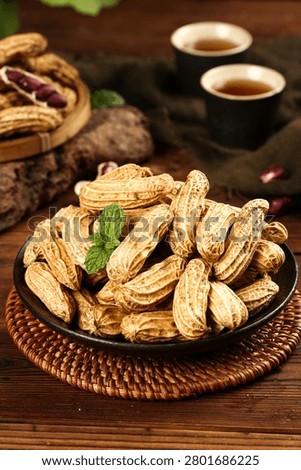 Fresh roasted peanuts in shell served on rustic wooden table with traditional Chinese tea cups, featuring mint garnish and warm ambient lighting
