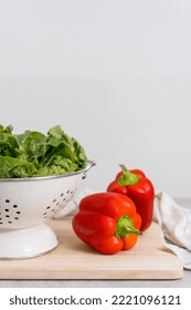 Fresh Romaine Lettuce In Metal Colander And Red Bell Pepper On Wooden Board On Worktop At Home Kitchen With Light Interior, Healthy Food