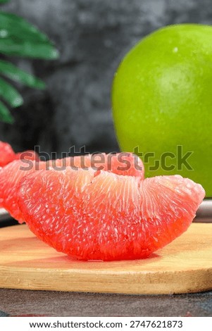 Fresh ruby red pomelo segment with tantalizing juicy flesh displayed on wooden board, green whole fruit in background, Thai tropical citrus style composition.