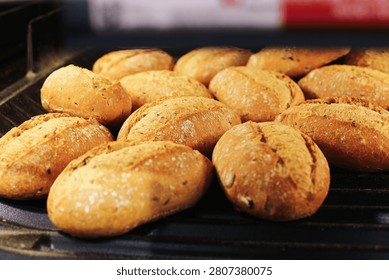 Fresh rustic bread rolls lie on bakery display tray. Golden crust covers small baked buns. Food background fits daily bread, bakery products, grocery shelves and breakfast meals. Simple food scene.