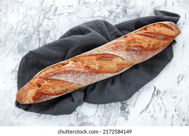 Fresh Rustic French Sourdough Baguette On Kitchen Towel On Marble Table, Top View. Free Space For Text