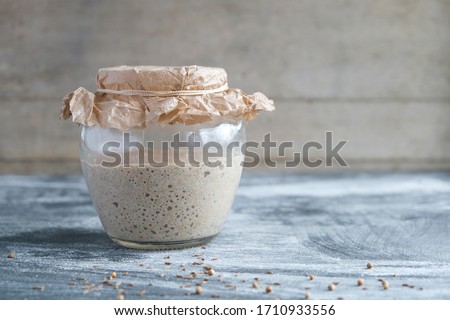 fresh rye sourdough on whole grain flour in glass jar, yeast-free leaven starter for healthy organic rustic bread, spices are scattered on table, copy space