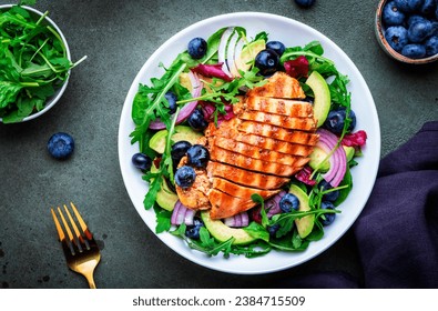 Fresh salad with blueberries, grilled chicken breast, avocado, red onion, walnuts and arugula on green table background, top view - Powered by Shutterstock