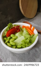 Fresh salad with carrot, tomato, edamame and lettuce served on the white bowl