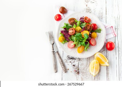 Fresh salad with cherry tomatoes, spinach, arugula, romaine and lettuce in a plate on white wooden background, top view - Powered by Shutterstock