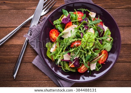 Fresh salad with chicken, tomatoes and mixed greens (arugula, mesclun, mache) on wooden background top view. Healthy food.