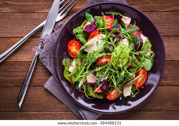 Fresh\
salad with chicken, tomatoes and mixed greens (arugula, mesclun,\
mache) on wooden background top view. Healthy\
food.