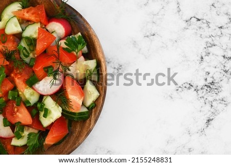 Fresh salad consisting of tomatoes, cucumbers, radishes, green onions, parsley, dill with olive oil, close-up, on a light marble natural background, copy space