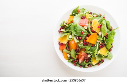 Fresh salad with fruits and greens on white wooden background top view with space for text. Healthy food.