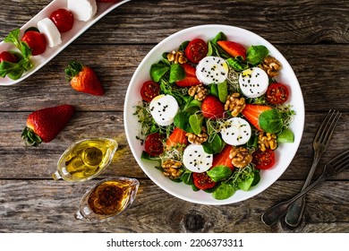 Fresh salad - goat cheese, strawberries, walnuts, cherry tomatoes and leafy greens on wooden table  - Powered by Shutterstock