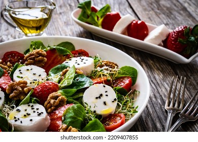 Fresh salad - goat cheese, strawberries, walnuts, cherry tomatoes and leafy greens on wooden table  - Powered by Shutterstock