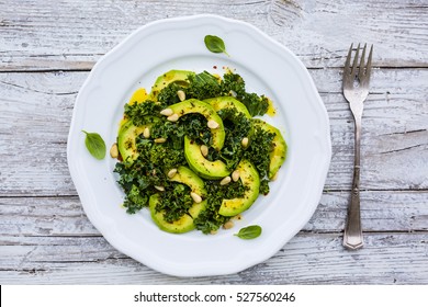 Fresh Salad With Kale Leaves And Avocado On A White Plate On Wooden Table.