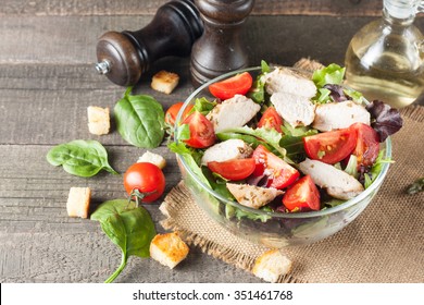 Fresh Salad Made Of Tomato, Ruccola, Chicken Breast, Arugula, Crackers And Spices. Salad In A White, Transparent Bowl On Wooden Background