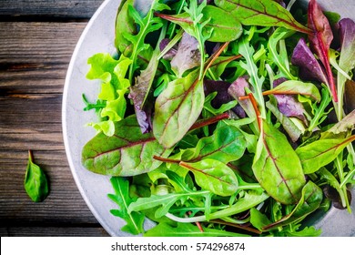 Fresh salad with mixed greens in bowl on wooden background closeup 