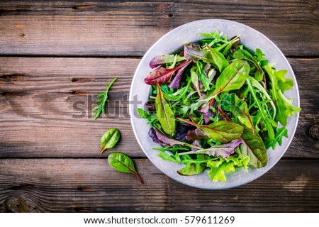 Fresh salad with mixed greens in bowl on wooden background