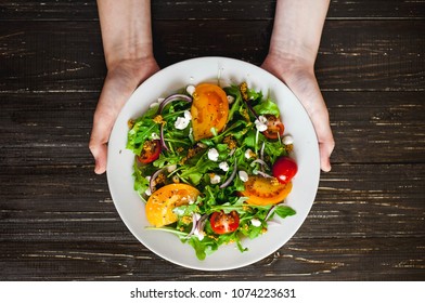 
fresh salad in
 a plate in holding hands on a wooden background