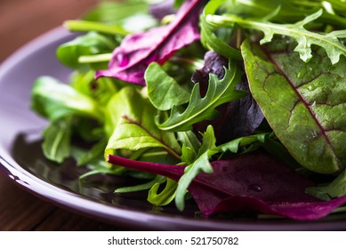 Fresh salad plate with mixed greens (arugula, mesclun, mache) on dark wooden background close up. Healthy food. Green meal.