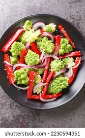 Fresh salad of steamed romanesco broccoli, bell pepper and red onion sprinkled with sesame seeds close-up in a plate on the table. Vertical top view from above

