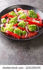 Fresh salad of steamed romanesco broccoli, bell pepper and red onion sprinkled with sesame seeds close-up in a plate on the table. Vertical

