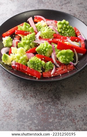 Fresh salad of steamed romanesco broccoli, bell pepper and red onion sprinkled with sesame seeds close-up in a plate on the table. Vertical