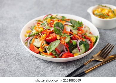 Fresh salad with vegetables. Arugula, spinach, cucumbers, tomato, onions carrots, corn andradishes in a plate on the table. Diet nutrition.  Copy space