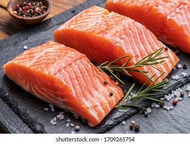 Fresh salmon fillets on black cutting board with herbs and spices.