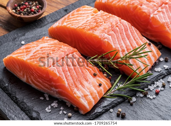 Fresh salmon fillets on black cutting board with\
herbs and spices.