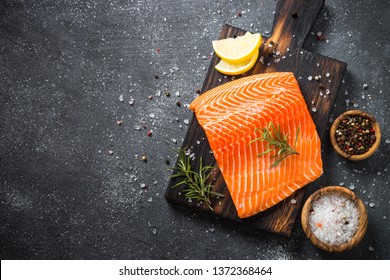 Fresh Salmon fish. Uncooked salmon fillet with ingredients for cooking on black stone table. Top view with copy space.