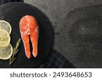 Fresh salmon steak, rosemary and lemon on dark textured table, top view. Space for text