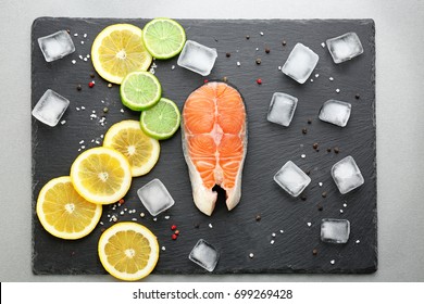 Fresh salmon steak with spices, citrus fruits and ice cubes on slate plate