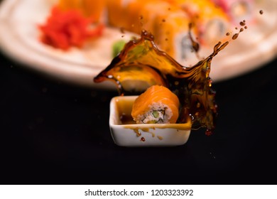 Fresh Salmon Sushi Roll Falling Into A Side Dish Of Soy Sauce With A Splash Of Liquid In A Freeze Motion