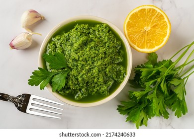 Fresh salsa verde in a bowl. Chimichurri dipping sauce from fresh parsley, garlic cloves, olive oil and lemon juice. Green sauce with fresh herb and spices. Healthy condiment recipe. Top view.