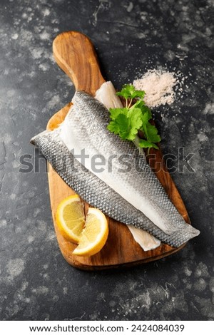 Fresh sea bass fillets on wooden board with herbs