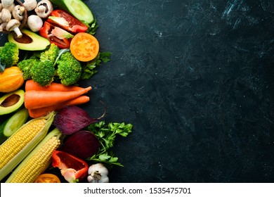 Fresh seasonal vegetables on a black stone background: Pumpkin, tomato, avocado, cucumber, onion, carrot. Autumn food. Top view. Free copy space.