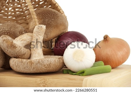 Fresh shiitake mushrooms, various onions on a wooden cutting board isolated on white background. Fungi recipes and medicinal herbs