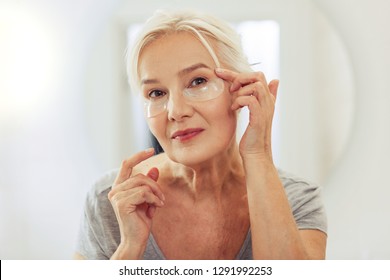 Fresh skin. Positive joyful woman applying eye patches on her face while wanting to have fresh skin - Powered by Shutterstock